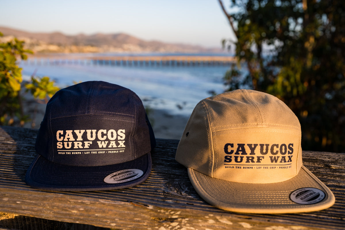 Pair of Cayucos Surf Wax flat brimmed jockey cap with adjustable closure