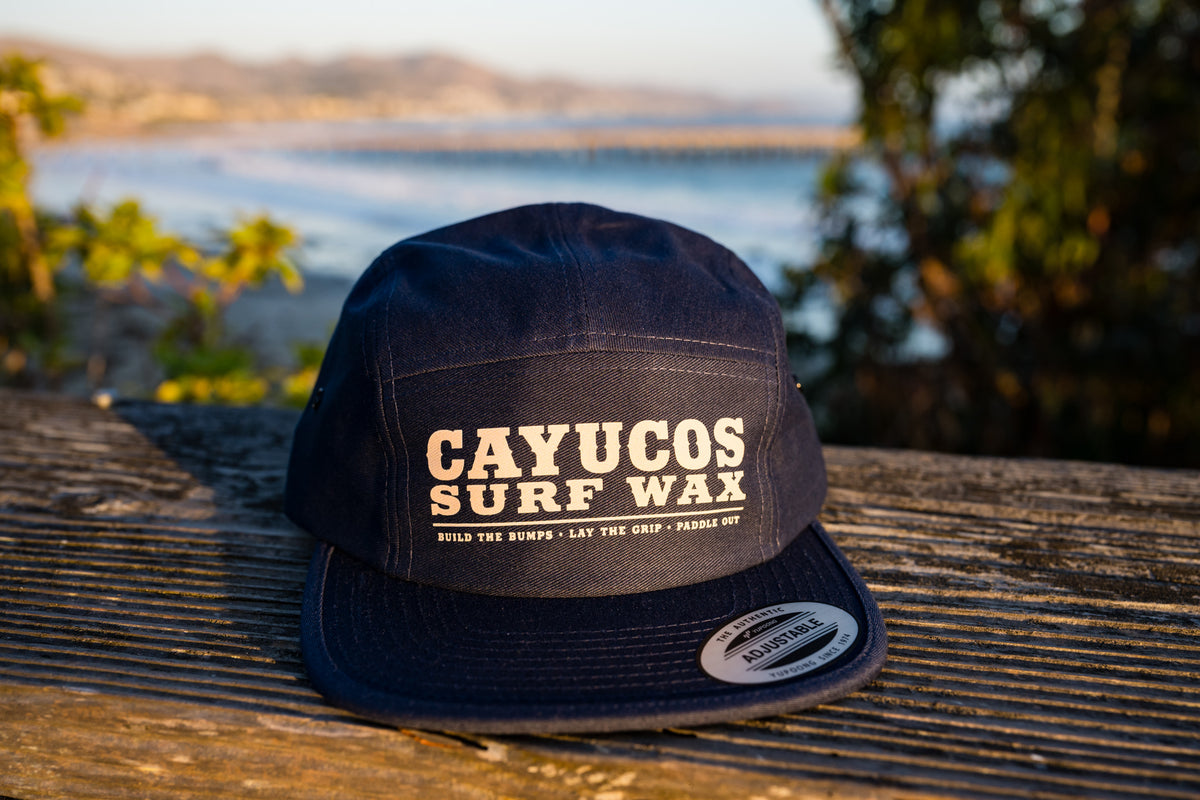 Front view of Cayucos Surf Wax navy blue flat brimmed jockey cap with adjustable closure