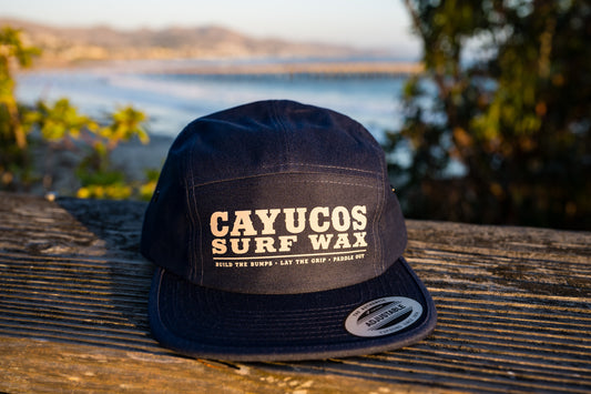 Front view of Cayucos Surf Wax navy blue flat brimmed jockey cap with adjustable closure