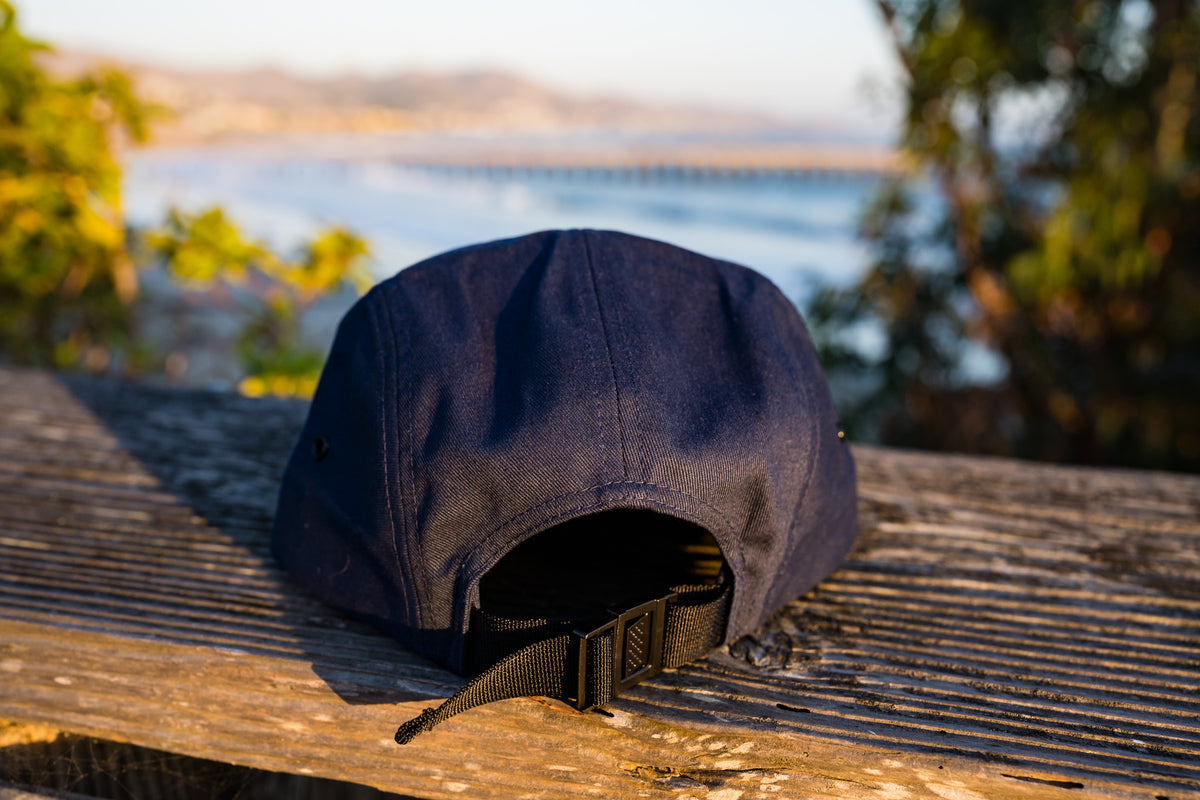 Back view of Cayucos Surf Wax navy blue flat brimmed jockey cap with adjustable closure